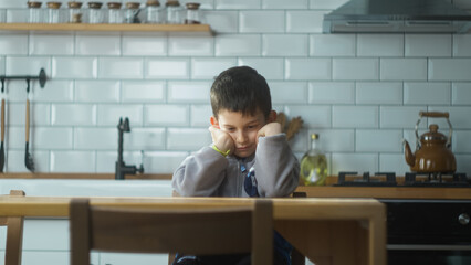 Upset kid sitting in kitchen alone at home. Lonely offended schoolboy feeling disappointed bullied,...