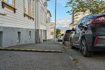 electric vehicle being recharged by plug across the sidewalk