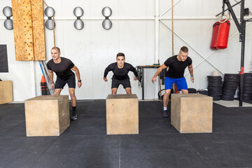 Fitness group performing box jumps at gym, plyometric exercise