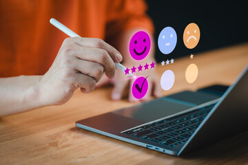 On a laptop, a customer selects a happy smile face icon on a virtual screen, signaling satisfaction in service. Concept of assessment, testimonial, customer service feedback, and opinion rating. - 760471697