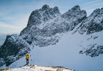 Adventurous man hiker on top of a steep rocky cliff overlooking winter alpine like moutain landscape of High Tatras, Slovakia. Alpine mountain landscape covered with glaciers, snow and ice.