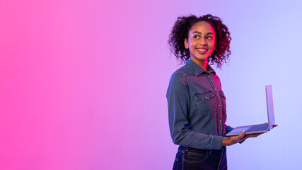 Smiling black woman holding laptop on vivid gradient backdrop, copy space