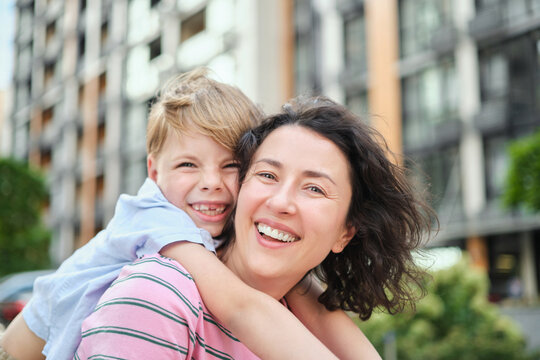 young mother and son smiling looking at the camera in modern residential complex. Having fun together, happy parenting, new home concept. Bright summer day in the urban background. High quality photo