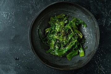 Fresh sautéed greens with sesame seeds in a dark bowl on a textured surface.