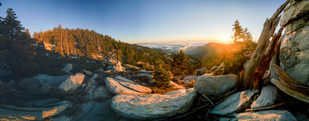 A panoramic view of a rocky mountain with a sun setting in the background