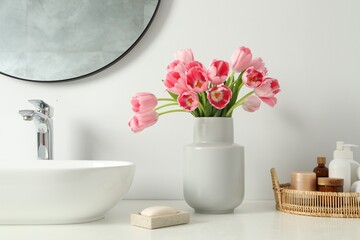 Vase with beautiful pink tulips and toiletries near sink in bathroom