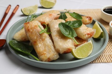 Plate with tasty fried spring rolls, spinach, arugula and lime on white table, closeup