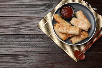 Tasty fried spring rolls and sauce served on wooden table, top view. Space for text
