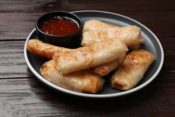 Tasty fried spring rolls and sauce on wooden table, closeup