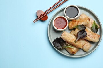 Tasty fried spring rolls, lettuce and sauces served on light blue table, top view. Space for text