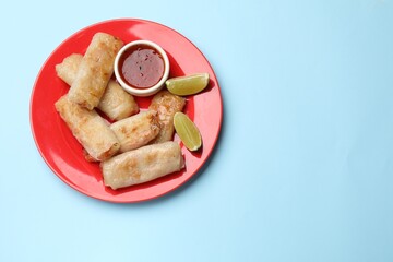 Tasty fried spring rolls, lime and sauce on light blue table, top view. Space for text