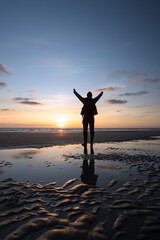 Fototapeta na wymiar Mann steht mit vor Freude hochgerissenen Armen im Wattenmeer am Nordsee Strand.