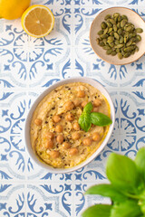 A bowl of hummus with chickpeas and basil on a table
