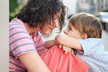 Adorable mother and son smiling happy having fun at city background. Motherhood concept, hugging. Boy 8 years old with mother in bright clothes enjoying summer day. High quality photo