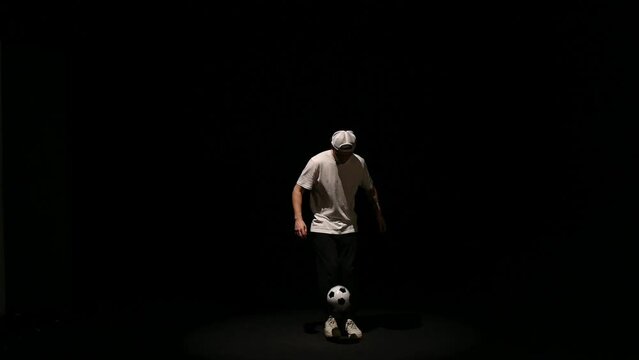 A young man throws a soccer ball on a black background. Football player shows tricks with the ball. Freestyler hits a black and white ball on a dark background. High quality FullHD footage