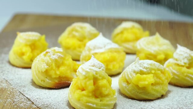 Profiteroles or cream puff with filling, falling powder sugar topping. Fresh homemade Cream Puffs, cake, tasty French choux puff, ecler, dessert closeup. Pastries