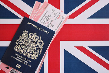 Blue British passport with airline tickets on national flag background close up. Tourism and travel concept