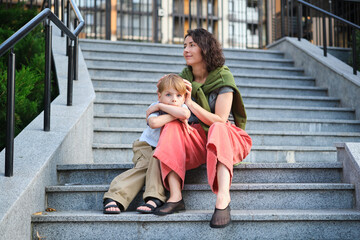 Happy family: mother and child son hugging and laugh sitting on the city stairs. motherhood...