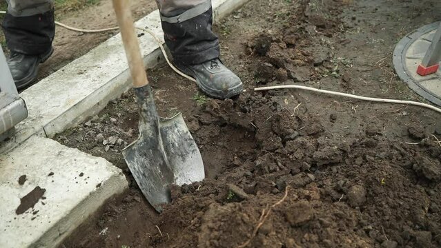 Worker Digs electric wires into the ground with a Shovel Man digs a ditch in the ground with a shovel