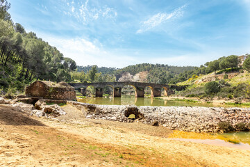 Fototapeta na wymiar Water mill in the shore of Odiel river and roman bridge in the background. Hiking route of the water mills along the Odiel river from Sotiel Coronada