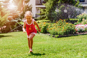 Having Fun Water Sprinkler Summer Vacations. Wet Little Girl Child Running Barefoot on Lawn under...