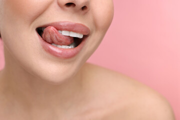 Fototapeta premium Woman with beautiful lips licking her teeth on pink background, closeup