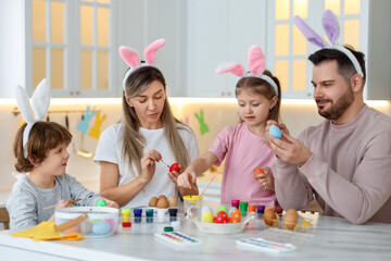 Easter celebration. Happy family with bunny ears painting eggs at white marble table in kitchen