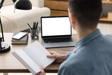 E-learning. Young man with book during online lesson at table indoors, closeup