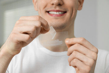 Young man with whitening strips indoors, closeup