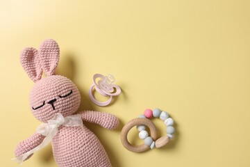 Baby accessories. Toy rabbit, pacifier and rattle on yellow background, flat lay. Space for text