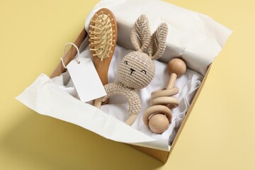 Different baby accessories and blank card in box on yellow background
