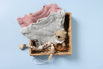 Different baby accessories and clothes in wicker box on light blue background, top view