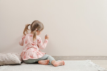 Little girl drawing on beige wall indoors, back view and space for text. Child`s art