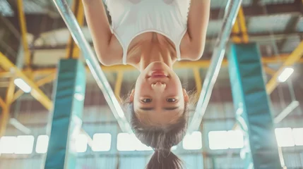 Fototapete asian female gymnast hanging upside down on the uneven bars in a bright gym  © cristian