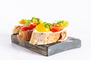 Bruschetta set with colorful tomatoes, aromatic herbs and cream cheese on rustic wooden board close up. Healthy tasty food concept.
