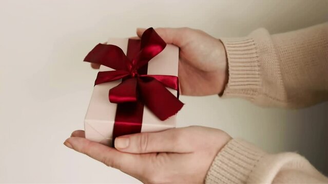 Woman hands holding the gift close up soft pink colors red ribbon