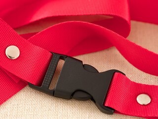 A black contoured side release plastic buckle with red nylon belt on a beige textile background