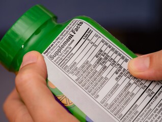 A close-up shot of a vitamin supplement jar with a supplement facts label at the back in woman hands