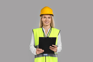 Engineer in hard hat holding clipboard on grey background