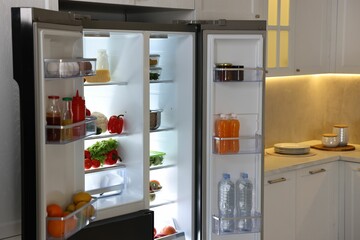 Open refrigerator full of different products in kitchen