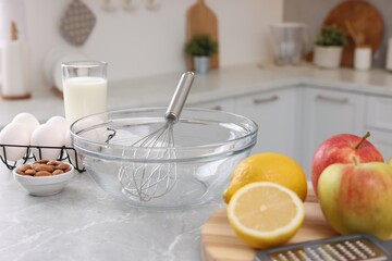 Metal whisk, bowl and different products on gray marble table in kitchen