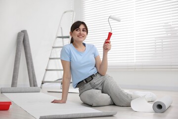 Woman with roller and wallpaper in room