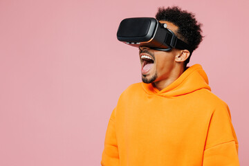 Young man of African American ethnicity wear yellow hoody casual clothes watching in vr headset pc gadget open mouth isolated on plain pastel light pink background studio portrait. Lifestyle concept.