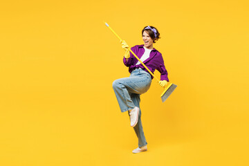 Full body young happy woman wears purple shirt casual clothes do housework tidy up hold in hand brush broom pov play guitar isolated on plain yellow background studio portrait. Housekeeping concept. - obrazy, fototapety, plakaty