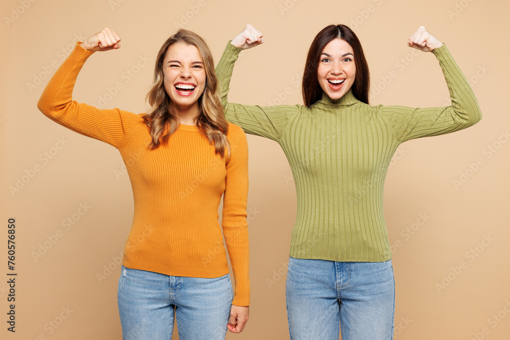 Poster Young friends two women they wear orange green shirt casual clothes together show biceps muscles on hand demonstrating strength power isolated on plain pastel light beige background Lifestyle concept