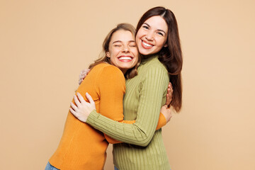 Side view young friends two women they wear orange green shirt casual clothes together hug cuddle embrace each other isolated on plain pastel light beige background studio portrait. Lifestyle concept.