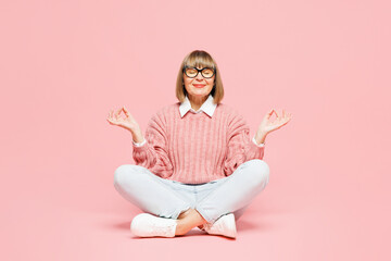Full body elderly woman 50s years old wear sweater shirt casual clothes glasses sits hold hands in yoga om aum gesture relax meditate try calm down isolated on plain pink background Lifestyle concept