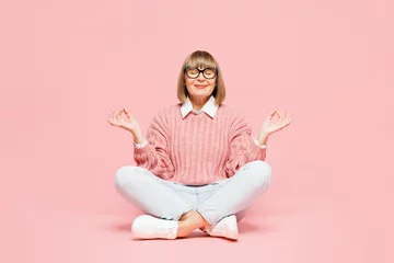 Fotobehang Full body elderly woman 50s years old wear sweater shirt casual clothes glasses sits hold hands in yoga om aum gesture relax meditate try calm down isolated on plain pink background Lifestyle concept © ViDi Studio