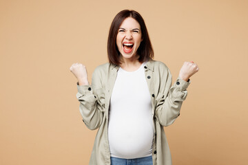 Young pregnant woman future mom wear grey shirt with belly stomach tummy with baby doing winner gesture celebrate clenching fists isolated on plain beige background Maternity family pregnancy concept