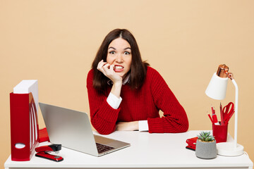 Young shocked stressed worried employee business woman wear red sweater shirt sit work at office...